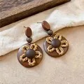 Gros plan sur les boucles d'oreilles vintage en bois et paille sur fond rustique - Pendentif Fleur en Bois (HE35489) / Aiguille en argent / Marron
