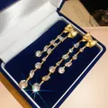 Detailansicht funkelnder Schleifen-Ohrringe mit Zirkonia-Steinen in einer blauen Box. - Schleife Quaste Stil (HE35609) / Gold