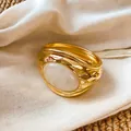 Makroansicht der komplizierten goldenen Faltentextur und des ovalen weißen Harzsteineinsatzes - Weißes Harz / Gold