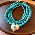 Detailopname van een meerlaagse turquoise kralenketting met een gouden harthanger - Gouden Hart Hanger Stijl / Blauw