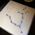 Gedetailleerde weergave van zilverkleurige ketting en oorbellen met blauwe bloemen - Ketting En Oorbellen Set / Zilver-Blauw