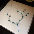 Gedetailleerd overzicht van groene strass bloem en blad ketting en oorbellen set in doos - Ketting En Oorbellen Set / Zilver-Hemelsblauw