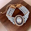 Nahaufnahme eines Vintage Mehrstrang-Perlenarmbands mit ovalem Kristall-Mittelstück - Vintage Oval Stück Mehrlagiges Armband / Gold-Weiß