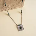 Gros plan d'un collier en acier inoxydable avec un pendentif carré en rubis zoisite sur pierre. - Argent-Vert
