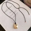 Detaillierte Makroansicht eines minimalistischen goldenen ovalen Anhängers an einer Kordel - Glänzendes Gold