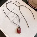 Minimalistische Lederhalskette mit mattem weinrotem ovalem Anhänger auf einem Buch. - Rot