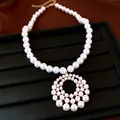 Detailansicht einer eleganten Perlenkette mit einem großen, runden, durchbrochenen Anhänger - Weiß
