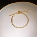 Detail van verstelbare gouden mesh armband met sprankelende zirconen op een wit bord. - Goud