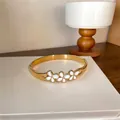 Vue rapprochée d'un élégant bracelet en acier doré avec des détails de fleurs en émail blanc - Relief Floral / Or-Blanc