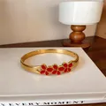 Gros plan d'un bracelet jonc en acier doré orné de trois fleurs en émail rouge. - Relief Floral / Or-Rouge