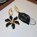 Detalle de pendientes asimétricos negros de flor y hoja con elegante baño de oro. - Asimétrico Flor y Hoja (HE35536) / Negro