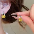 Nahaufnahme von eleganten Blumen-Ohrhängern mit gelbem Zirkon, am Ohr getragen und gehalten - Ohrringe Nur / Gelb