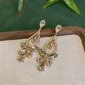 Detailansicht eleganter goldener Ohrringe mit funkelnden Strass-Tropfenanhängern. - Weiß