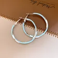 Elégantes créoles torsadées en émail bleu clair sur un fond en cuir marron texturé. - Créoles Torsadées / Argent-Bleu