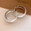 Vue détaillée de boucles d'oreilles créoles en émail blanc sur un fond en cuir raffiné. - Créoles Torsadées / Argent-Blanc