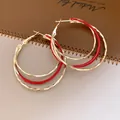 Gros plan détaillé de boucles d'oreilles créoles dorées torsadées avec un émail rouge élégant - Créoles Torsadées / Or-Rouge