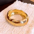 Gros plan d'un jonc ovale doré ondulé avec finition texturée vintage et charnière. - Style de Texture Ondulée / Or