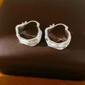 Detalle de pendientes de aro plateados con diseño plisado sobre estuche de cuero marrón. - Estilo Redondo Plisado / Plateado