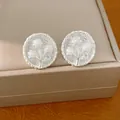 Detailopname van zilverkleurige ronde oorknopjes met bloem- en pareldetail - Bloemvorm / Zilver/Wit