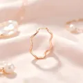 Gros plan macro d'une bague vague minimaliste en or rose sur un fond de tissu rose soyeux - Or rose