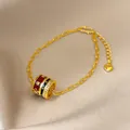 Close-up of 24K gold plated cylinder charm bracelet with red enamel and zircons. - Gold-Red