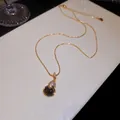 Gros plan d'un collier plaqué or 18 carats avec pendentif Wu Lou serti de zircons - Or avec Café