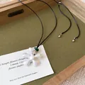 Detalle de un collar con colgante de flor geométrica en blanco mate sobre tarjeta elegante - Flor