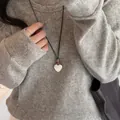 Détail d'un collier avec pendentif en forme de cœur brossé argenté sur un pull gris. - Cœur Brossé