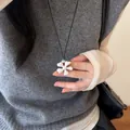 Gros plan détaillé d'un pendentif fleur blanche sur un collier de cordon noir porté par un mannequin - Fleur Brossée