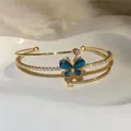 Detalle de brazalete abierto dorado con mariposa de cristal azul y circonitas brillantes. - Brazalete Abierto Mariposa (HB6979) / Dorado-Azul