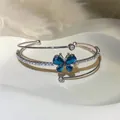 Detalle de brazalete abierto multicapa con mariposa de cristal azul y circonitas brillantes. - Brazalete Abierto Mariposa (HB6979) / Plata-Azul