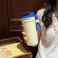 Close-up of a portable cream insulated coffee tumbler with blue lid held by hand - 550ml / Creamy White With Blue Lid