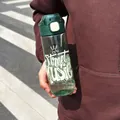 Close-up of a trendy green sports water bottle with Street Music print held in an outdoor setting - 700ml / Green/White