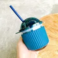 Close-up view of a minimalist blue egg-shaped glass cup with a silicone sleeve and straw - 350ml / Blue