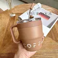 Nahaufnahme eines braunen Edelstahl-Kaffeebechers mit Strohhalm und Griff auf Holztisch - 480ml / Braun