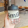 Close-up view of a transparent plastic coffee cup with a beige Smile fabric sleeve. - 500ml / Black