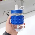 Close-up view of clear glass straw water bottle with blue heart pop-it silicone sleeve - 400ml / Blue