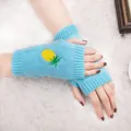 Gros plan sur des mitaines en tricot bleu clair avec une broderie d'ananas jaune - Taille unique / Bleu clair