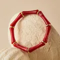 Primer plano de una pulsera de acrílico rojo con diseño de bambú y aros oro. - Rojo