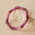 Primer plano de pulsera de acrílico púrpura con anillos dorados sobre piedra coral. - Púrpura