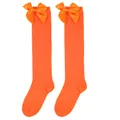 Detail of bright orange girls' knee-high socks featuring a large decorative satin bow. - Kids (7-12 Years) / Solid Orange/Orange Bow