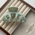 Detail of a sage green marble hair claw clip placed in a wooden jewelry box. - Green