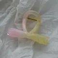 Close-up of small pink and yellow marbled hair claw clip on white textured paper - Smudged Bow Tie