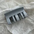 Primer plano detallado de una pinza para el pelo gris sobre fondo de papel - Gris