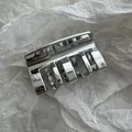 Vista detallada de una elegante pinza para el cabello plateada sobre papel arrugado - Plateado