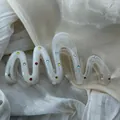 Detailed macro view of a wavy white hair claw clip accented with vibrant colorful rhinestones - Wave