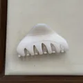 Detail view of a minimalist cream triangular hair claw clip on a soft beige display mat. - Fruit White