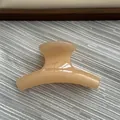 Close-up view of a small beige jelly-textured curved hair claw clip on textured grey fabric - Fruit Yellow