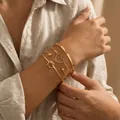 Primer plano de un set de cuatro pulseras doradas con diseños de corazón, nudo y cuentas - Juego de Cuatro Brazaletes Abiertos con Nudo de Corazón (DTZ81) / Dorado