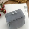 Detail view of small white pearl stud earrings on a grey velvet display box - Single Stud Style